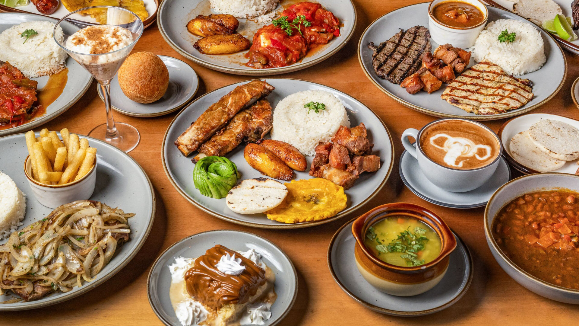 Mesa llena de platos colombianos: bandeja paisa, sancocho, arepas, empanadas y café